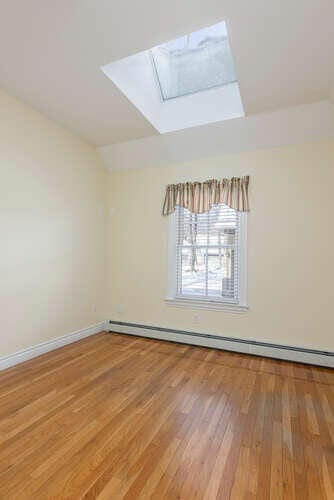 spare room with baseboard heating, lofted ceiling with skylight, and hardwood / wood-style flooring