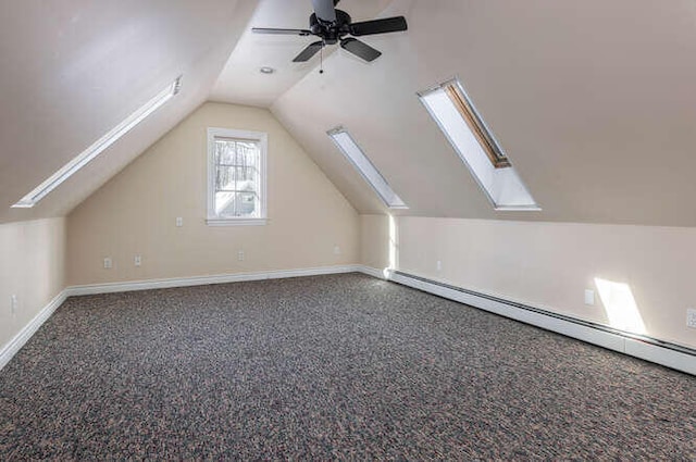 bonus room with dark colored carpet, a baseboard heating unit, vaulted ceiling with skylight, and ceiling fan