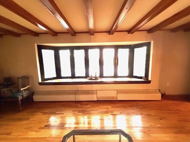 interior space with beam ceiling, baseboard heating, and light wood-type flooring