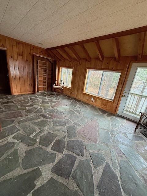 interior space featuring vaulted ceiling with beams, a healthy amount of sunlight, and wooden walls