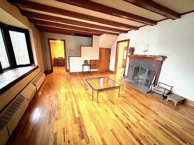 unfurnished living room with beam ceiling, radiator heating unit, a baseboard heating unit, and light hardwood / wood-style flooring