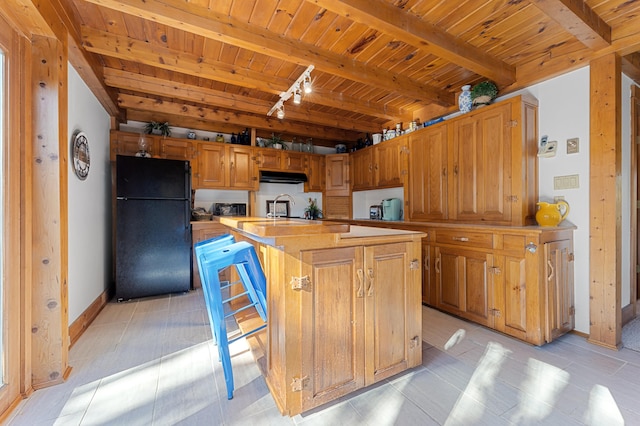 kitchen featuring light tile patterned flooring, a center island with sink, beam ceiling, wood ceiling, and black refrigerator