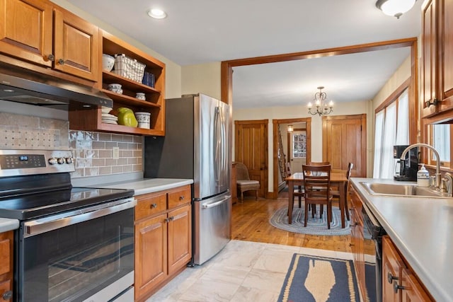 kitchen with appliances with stainless steel finishes, light wood-type flooring, sink, a notable chandelier, and hanging light fixtures