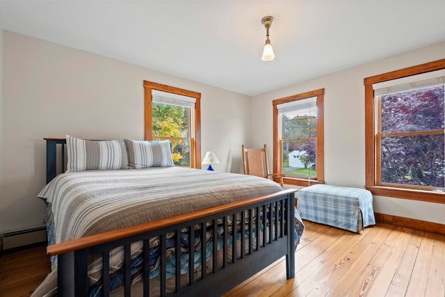 bedroom featuring light hardwood / wood-style flooring, multiple windows, and a baseboard heating unit