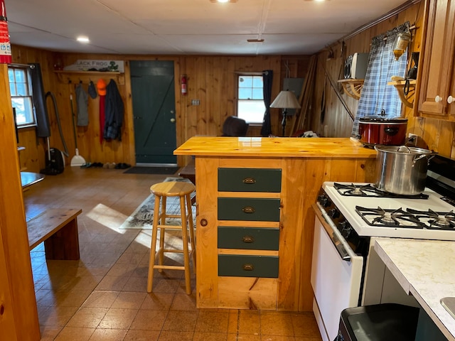 kitchen with white range with gas stovetop, a breakfast bar area, and wood walls