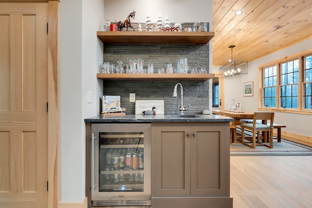 bar featuring wine cooler, hanging light fixtures, backsplash, light hardwood / wood-style floors, and sink