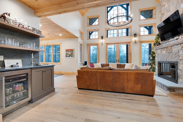 living room featuring wine cooler, a stone fireplace, light wood-type flooring, and wooden ceiling