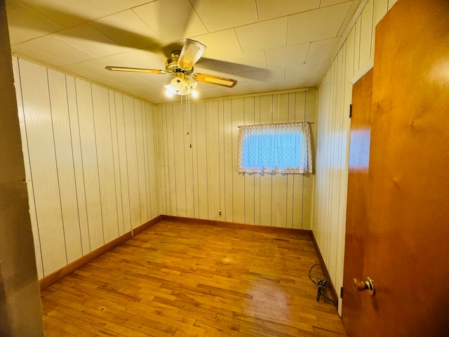 unfurnished room with wooden walls, light wood-type flooring, and ceiling fan