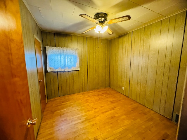 empty room featuring ceiling fan, light hardwood / wood-style flooring, and wooden walls