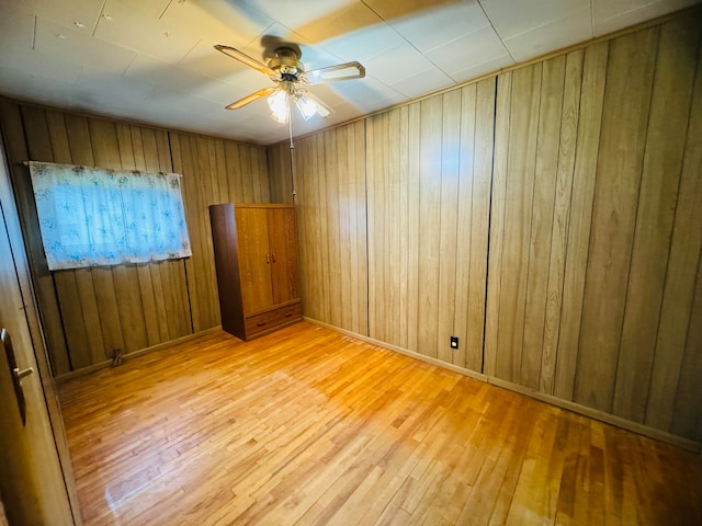 unfurnished room featuring light hardwood / wood-style floors, wood walls, and ceiling fan