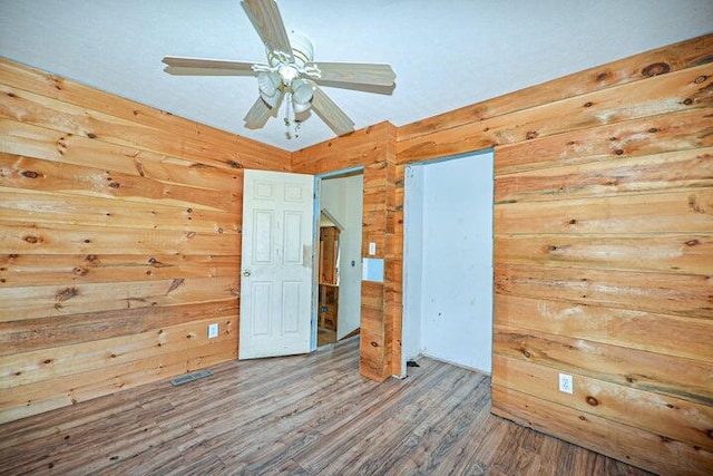 unfurnished bedroom with hardwood / wood-style flooring, wooden walls, and ceiling fan