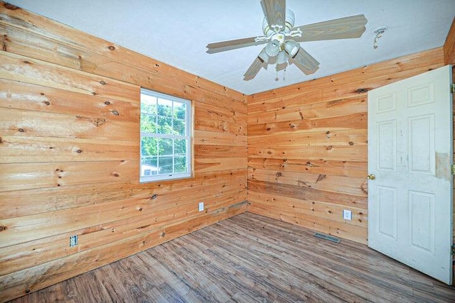 spare room featuring ceiling fan, wood walls, and hardwood / wood-style floors