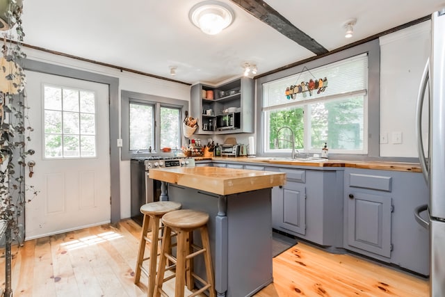 kitchen featuring sink, light wood-type flooring, butcher block counters, a kitchen breakfast bar, and stainless steel appliances