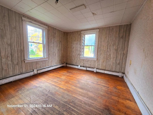 empty room featuring wood walls, wood-type flooring, and a baseboard radiator