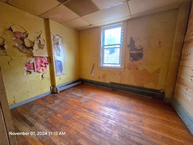 empty room with a paneled ceiling, baseboard heating, and dark hardwood / wood-style flooring