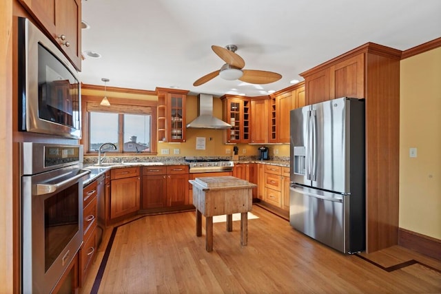 kitchen with pendant lighting, stainless steel appliances, wall chimney exhaust hood, and light hardwood / wood-style floors