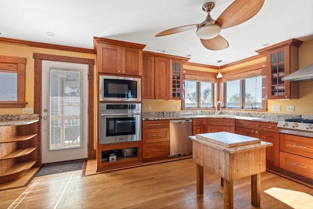 kitchen featuring stainless steel appliances, light hardwood / wood-style floors, crown molding, and light stone counters