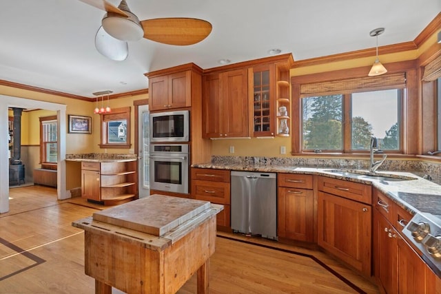 kitchen with a wood stove, hanging light fixtures, crown molding, light wood-type flooring, and appliances with stainless steel finishes