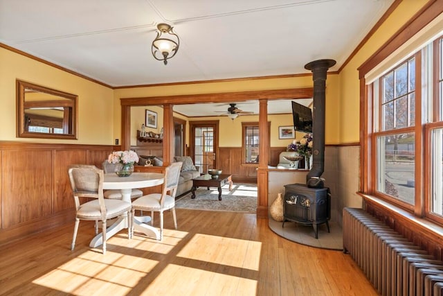 dining space with radiator heating unit, ornamental molding, a wood stove, ceiling fan, and light hardwood / wood-style flooring