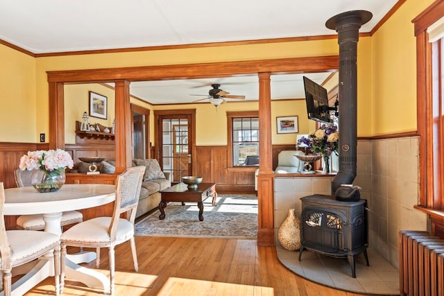 dining space with ornamental molding, ceiling fan, radiator heating unit, light hardwood / wood-style flooring, and a wood stove