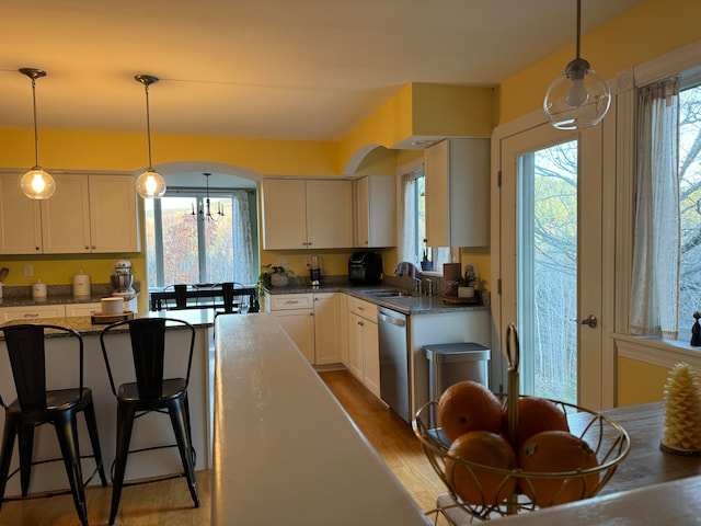 kitchen with wood-type flooring, white cabinetry, dark stone counters, stainless steel dishwasher, and pendant lighting