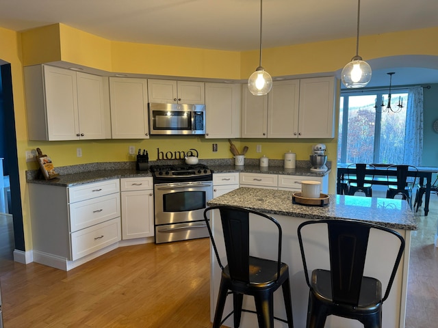 kitchen featuring hanging light fixtures, stainless steel appliances, light wood-type flooring, and dark stone counters