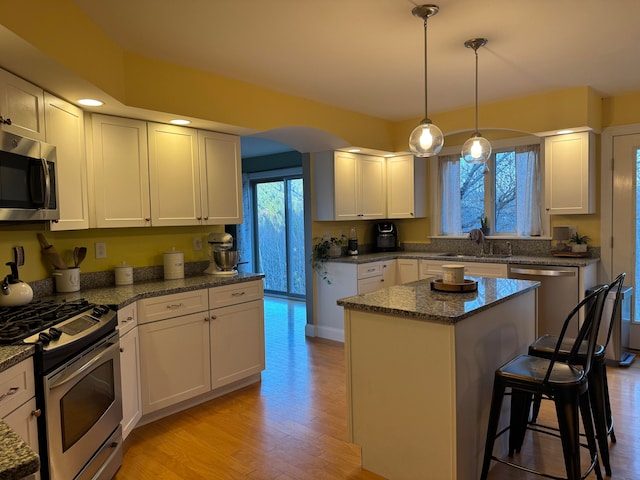 kitchen featuring light stone countertops, appliances with stainless steel finishes, light wood-type flooring, a kitchen island, and white cabinets