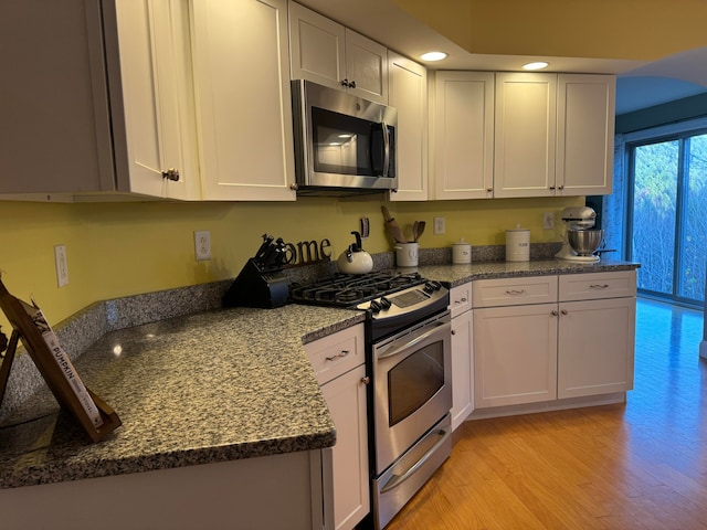 kitchen with appliances with stainless steel finishes, dark stone counters, light wood-type flooring, and white cabinets