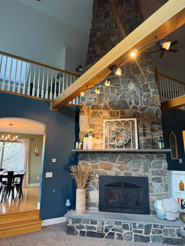 carpeted living room with a notable chandelier, a stone fireplace, and a high ceiling