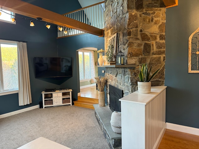 living room featuring beam ceiling, a stone fireplace, a towering ceiling, and hardwood / wood-style floors