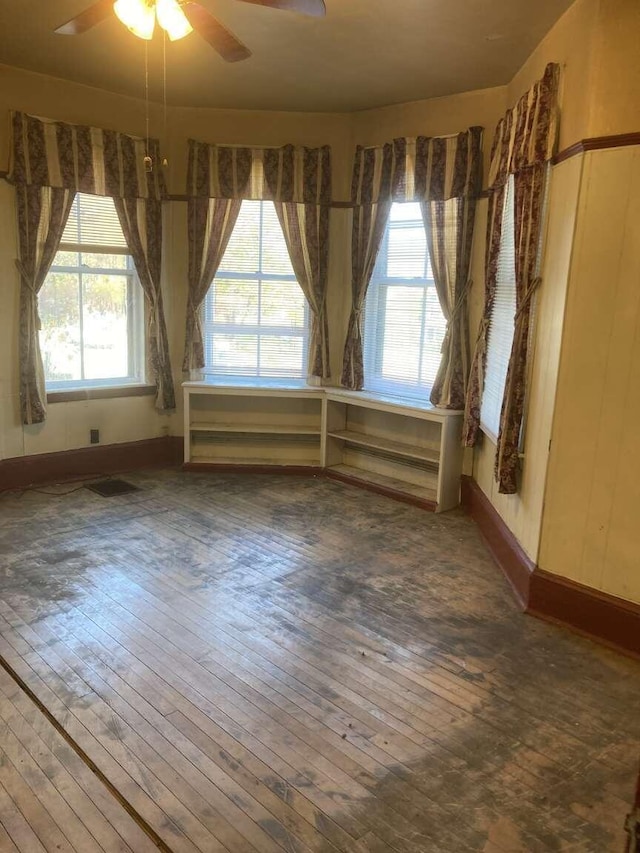 empty room featuring ceiling fan, dark wood-type flooring, and a wealth of natural light