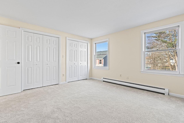 unfurnished bedroom with baseboard heating, multiple closets, light colored carpet, and multiple windows