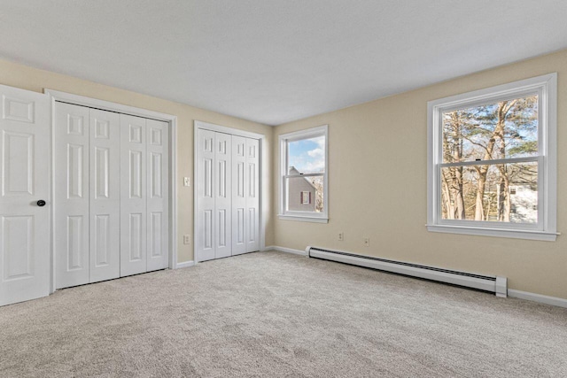 unfurnished bedroom featuring light colored carpet, baseboard heating, and multiple closets