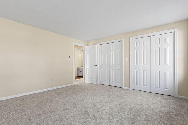 unfurnished bedroom featuring multiple closets and light colored carpet