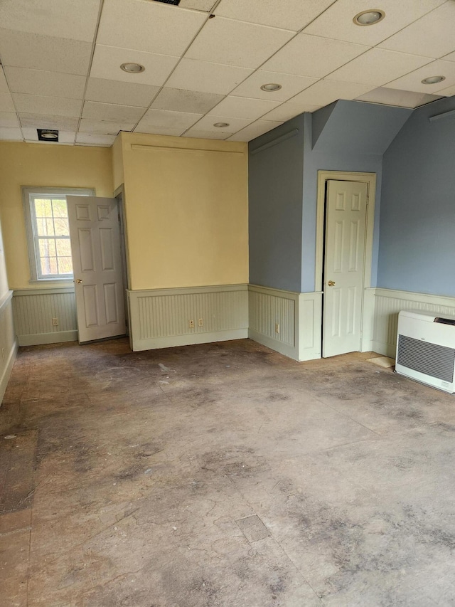 spare room with heating unit, a drop ceiling, and concrete flooring