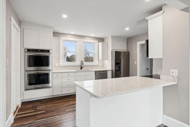 kitchen with sink, dark hardwood / wood-style floors, kitchen peninsula, white cabinets, and appliances with stainless steel finishes