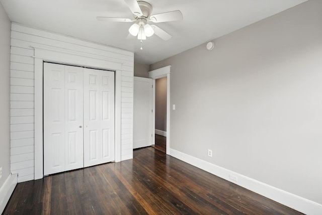 unfurnished bedroom with ceiling fan, a closet, dark wood-type flooring, and wood walls