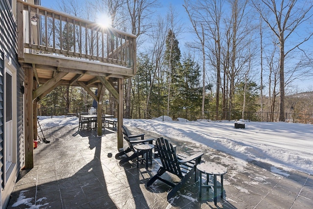 snow covered patio with a wooden deck, outdoor dining space, and fence