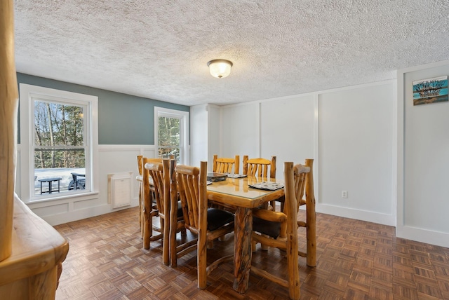 dining room featuring plenty of natural light, a wainscoted wall, a textured ceiling, and a decorative wall