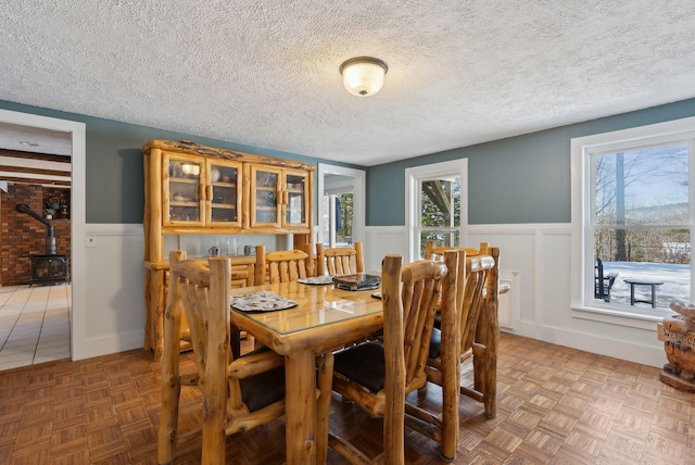 dining room featuring a wood stove, a textured ceiling, and a wainscoted wall