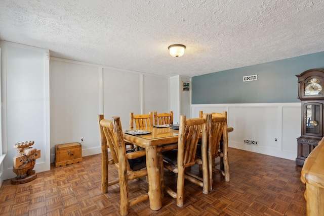 dining space featuring a textured ceiling, visible vents, a decorative wall, and wainscoting