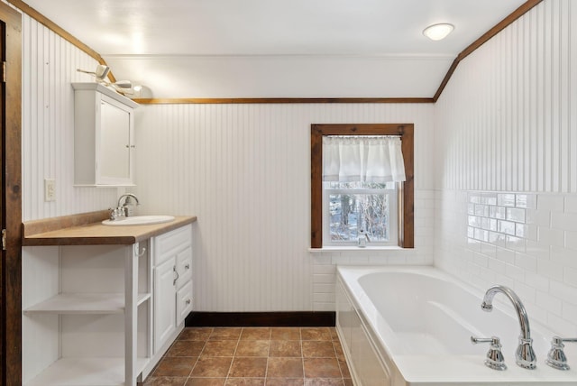 bathroom featuring baseboards, a garden tub, vanity, and ornamental molding