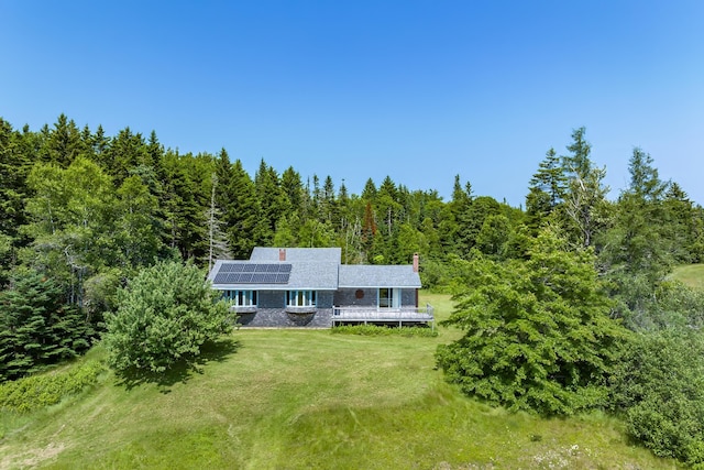 246 Marsh Stream Ln, Machiasport, ME 04655 - view of front of house featuring solar panels, a front yard, a forest view, a deck, and a chimney