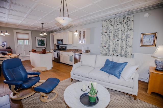 living room with an inviting chandelier, light hardwood / wood-style flooring, sink, and radiator