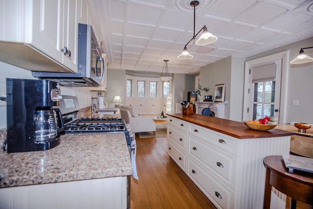 kitchen featuring appliances with stainless steel finishes, butcher block countertops, hardwood / wood-style floors, white cabinetry, and pendant lighting