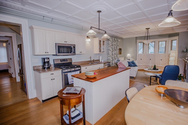 kitchen with stainless steel appliances, decorative light fixtures, light wood-type flooring, and white cabinets