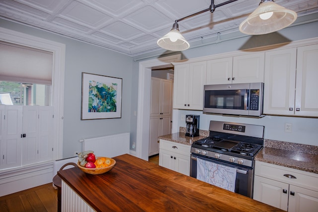 kitchen with appliances with stainless steel finishes, decorative light fixtures, white cabinets, and wood counters