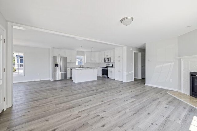 unfurnished living room featuring baseboards, light wood-type flooring, a fireplace, and a healthy amount of sunlight