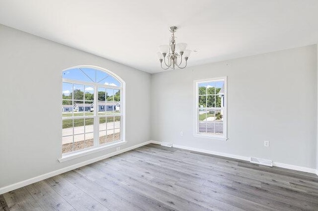 empty room featuring baseboards, a notable chandelier, and wood finished floors