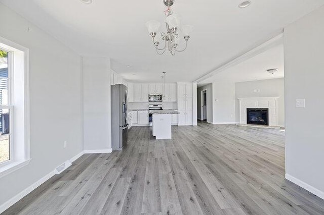 unfurnished living room featuring baseboards, a notable chandelier, light wood-style floors, and a healthy amount of sunlight